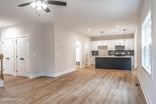 kitchen featuring light wood-type flooring, appliances with stainless steel finishes, white cabinets, decorative backsplash, and baseboards