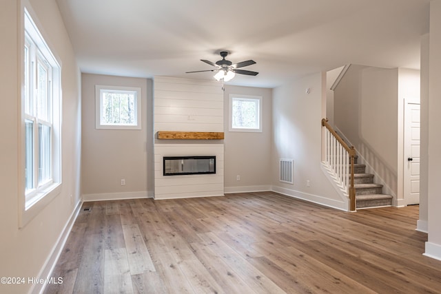 unfurnished living room with visible vents, wood finished floors, stairway, a large fireplace, and a healthy amount of sunlight