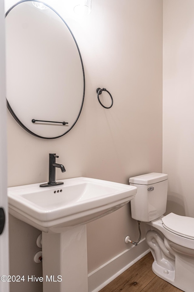 half bathroom featuring a sink, baseboards, toilet, and wood finished floors