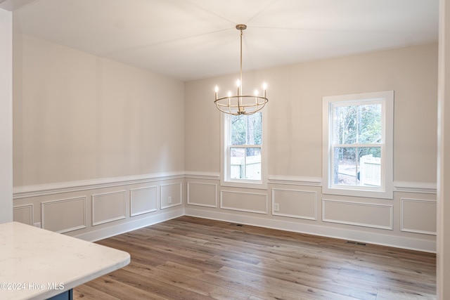 unfurnished dining area featuring plenty of natural light, wood finished floors, visible vents, and a chandelier