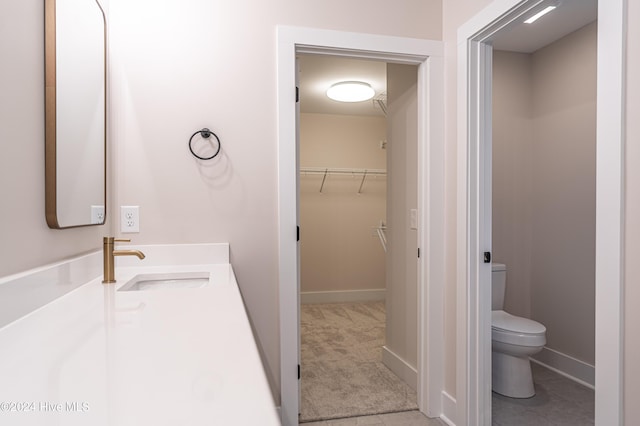 bathroom featuring vanity, baseboards, a spacious closet, tile patterned floors, and toilet