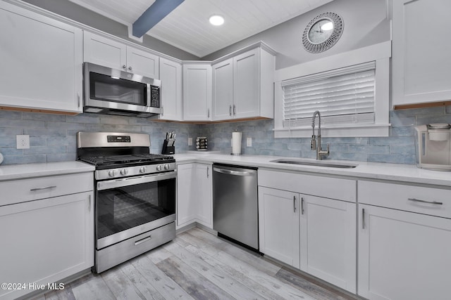 kitchen featuring beam ceiling, sink, light hardwood / wood-style flooring, appliances with stainless steel finishes, and white cabinets