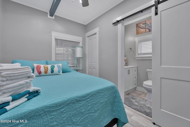 bedroom featuring ceiling fan, beam ceiling, a barn door, and light wood-type flooring