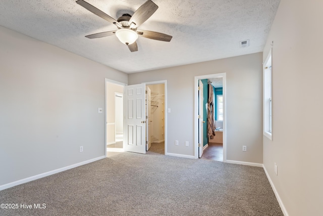 unfurnished bedroom with ceiling fan, carpet, connected bathroom, a textured ceiling, and a spacious closet