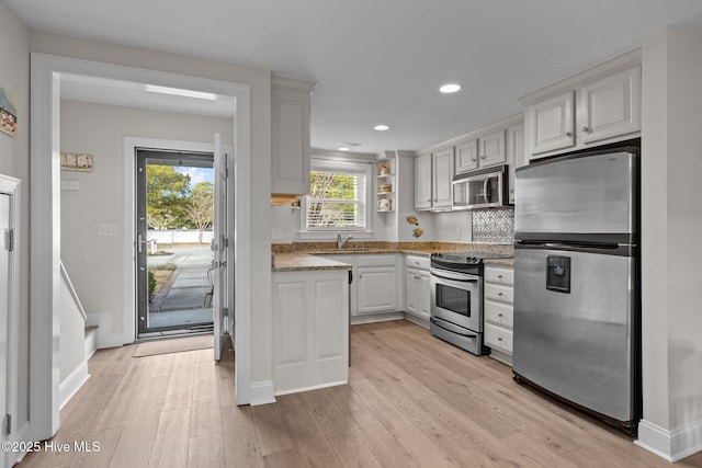 kitchen featuring white cabinetry, sink, stainless steel appliances, tasteful backsplash, and light hardwood / wood-style floors