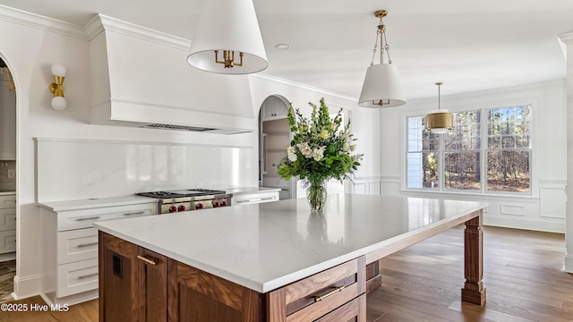 kitchen featuring light wood-type flooring, light stone countertops, pendant lighting, white cabinets, and stove