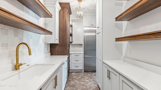 kitchen with sink, built in fridge, decorative light fixtures, white cabinets, and light stone countertops