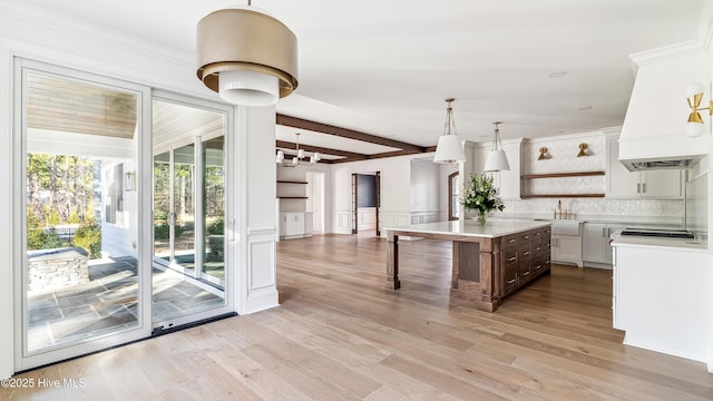 kitchen with decorative light fixtures, a kitchen island, backsplash, white cabinetry, and sink