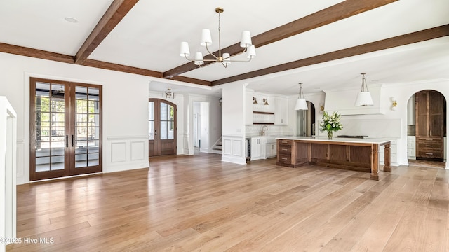 unfurnished living room featuring sink, french doors, an inviting chandelier, and light hardwood / wood-style floors