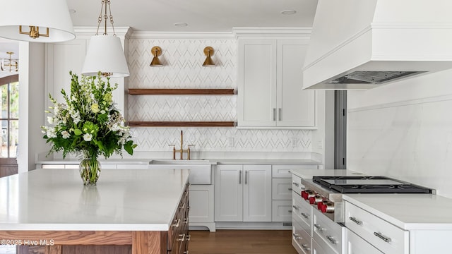 kitchen with decorative light fixtures, custom range hood, stainless steel gas cooktop, white cabinetry, and sink