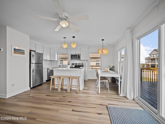 kitchen featuring appliances with stainless steel finishes, tasteful backsplash, white cabinets, light hardwood / wood-style floors, and a kitchen island