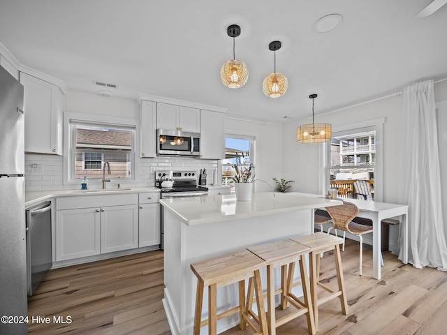 kitchen featuring stainless steel appliances, sink, decorative light fixtures, white cabinets, and light hardwood / wood-style floors