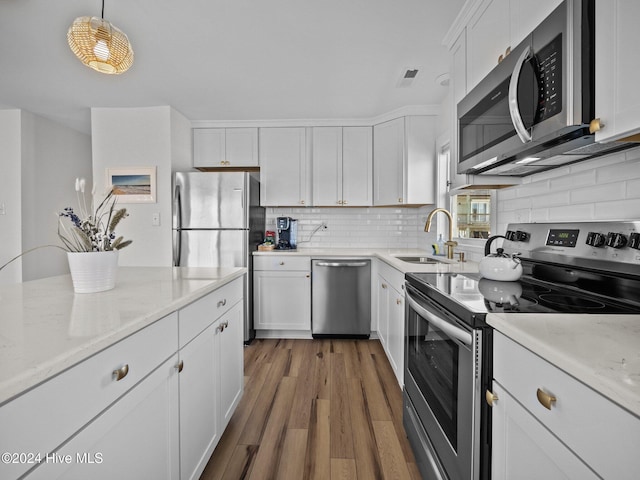 kitchen featuring sink, stainless steel appliances, wood-type flooring, decorative light fixtures, and white cabinets