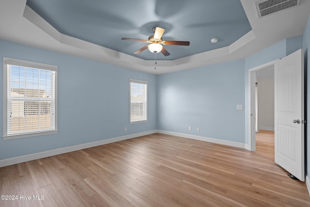 spare room with a tray ceiling, ceiling fan, and light hardwood / wood-style floors