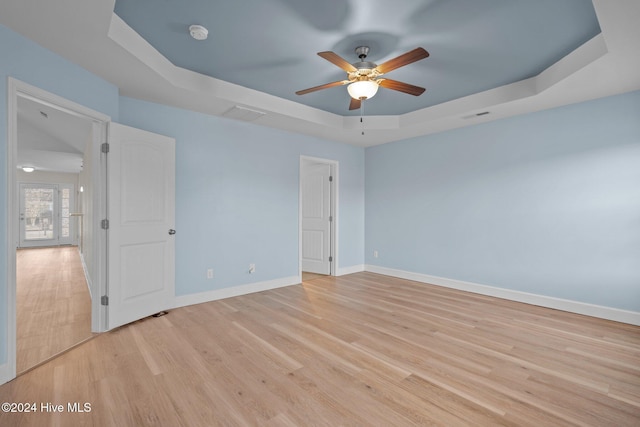 unfurnished room with french doors, light wood-type flooring, a tray ceiling, and ceiling fan