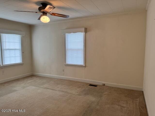 empty room featuring carpet flooring, a ceiling fan, baseboards, visible vents, and ornamental molding