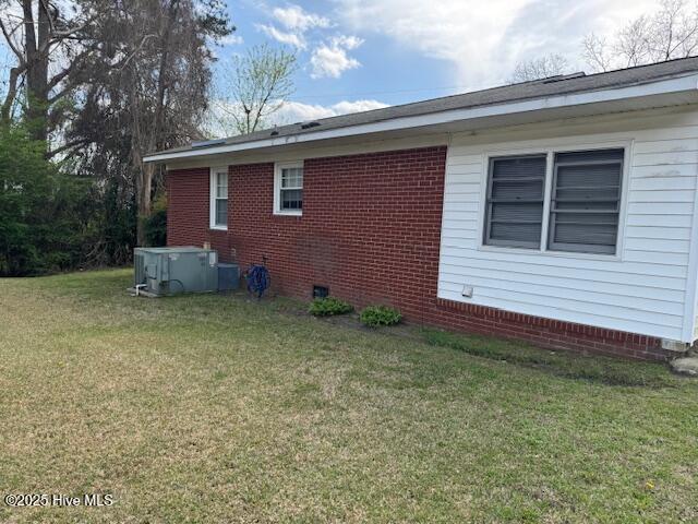 view of side of home with brick siding, central AC, and a yard