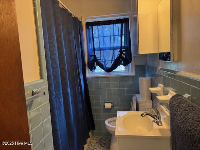 bathroom with a shower with curtain, tile walls, toilet, a wainscoted wall, and a sink