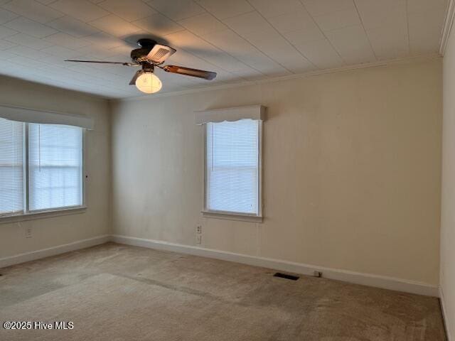 carpeted empty room with baseboards, a ceiling fan, visible vents, and crown molding