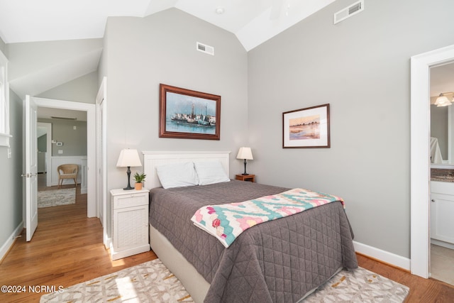 bedroom with vaulted ceiling, ensuite bathroom, and light wood-type flooring