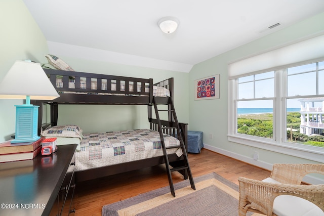 bedroom with vaulted ceiling, a water view, and light wood-type flooring