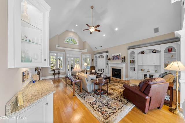 living room featuring a tile fireplace, ceiling fan, light hardwood / wood-style flooring, and high vaulted ceiling