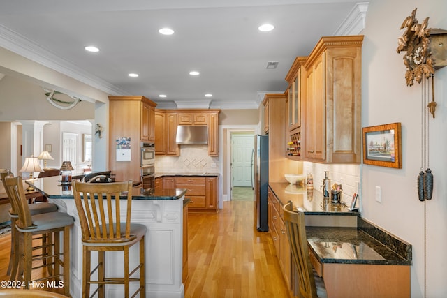 kitchen with stainless steel refrigerator, a kitchen breakfast bar, decorative columns, dark stone counters, and light hardwood / wood-style floors