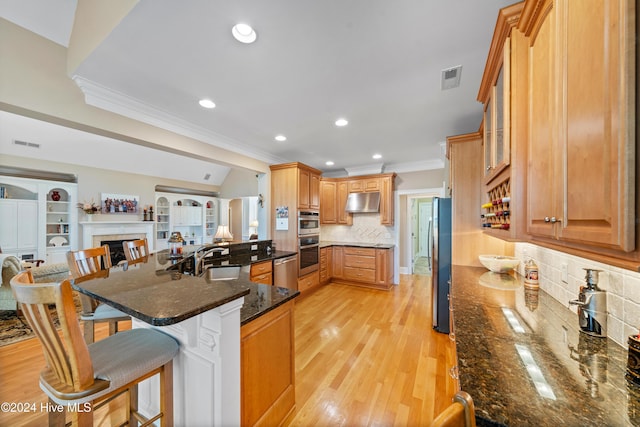 kitchen featuring a kitchen bar, tasteful backsplash, dark stone counters, sink, and light hardwood / wood-style flooring