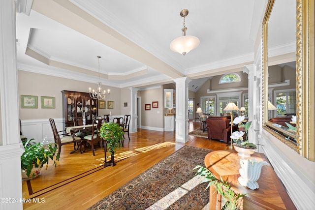 interior space featuring a raised ceiling, ornate columns, ornamental molding, wood-type flooring, and a chandelier