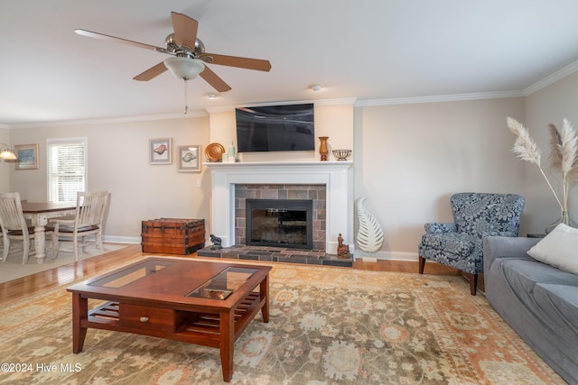 living room featuring a tiled fireplace, ceiling fan, crown molding, and wood-type flooring