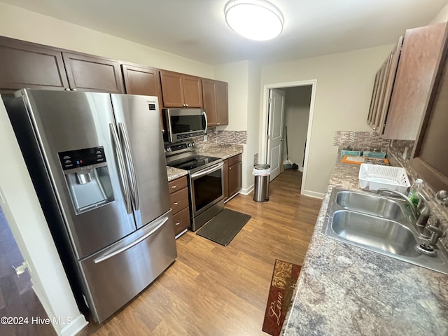 kitchen featuring light stone countertops, appliances with stainless steel finishes, backsplash, sink, and light hardwood / wood-style floors