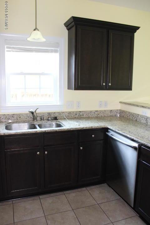 kitchen featuring pendant lighting, sink, stainless steel dishwasher, light tile patterned floors, and light stone counters