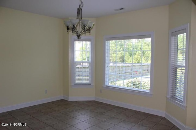 empty room with dark tile patterned floors and an inviting chandelier