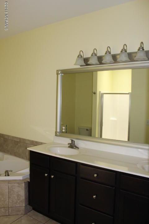 bathroom with tile patterned floors, a relaxing tiled tub, toilet, and vanity