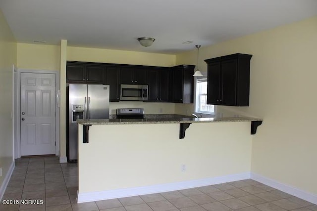 kitchen featuring kitchen peninsula, decorative light fixtures, a kitchen bar, light tile patterned floors, and appliances with stainless steel finishes