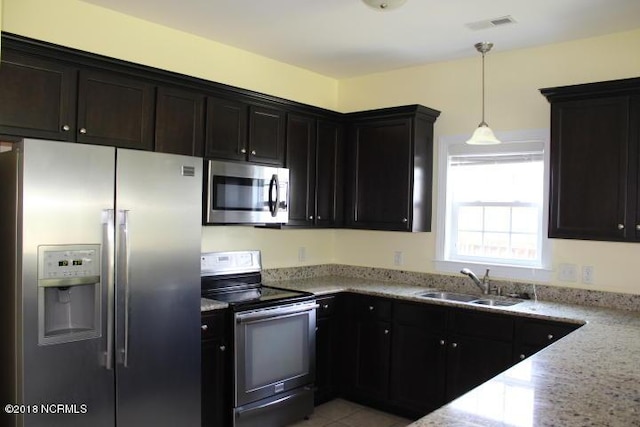 kitchen with decorative light fixtures, light stone counters, sink, and appliances with stainless steel finishes