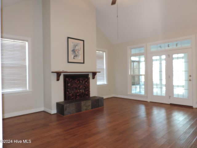 unfurnished living room with wood-type flooring, high vaulted ceiling, a healthy amount of sunlight, and a tiled fireplace