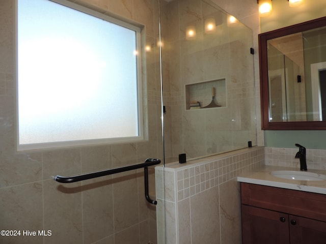 bathroom with vanity, a healthy amount of sunlight, an enclosed shower, and tile walls