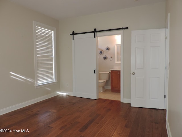 unfurnished bedroom featuring ensuite bathroom, a barn door, and dark hardwood / wood-style flooring