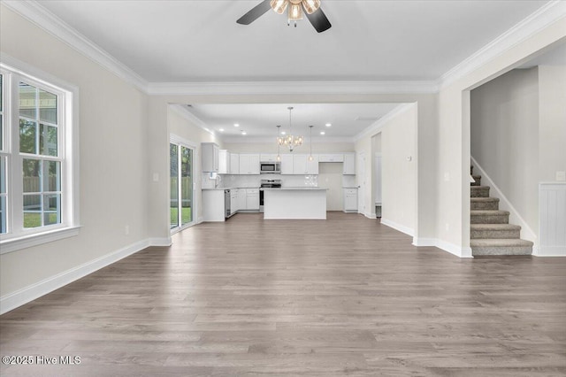 unfurnished living room featuring wood finished floors, crown molding, baseboards, and ceiling fan with notable chandelier