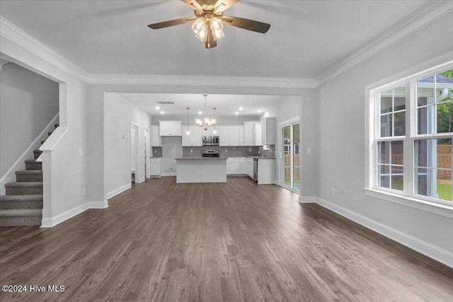 unfurnished living room with ceiling fan with notable chandelier, a healthy amount of sunlight, and dark hardwood / wood-style floors