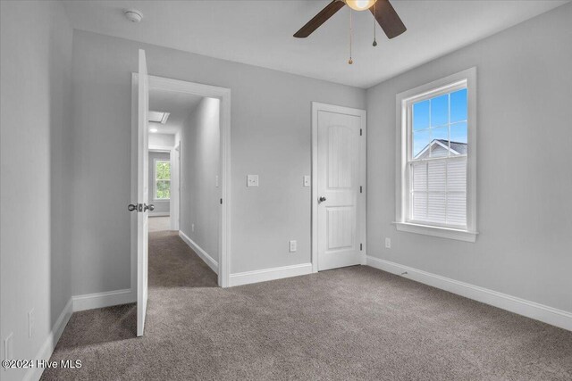 unfurnished bedroom featuring dark colored carpet, multiple windows, and ceiling fan