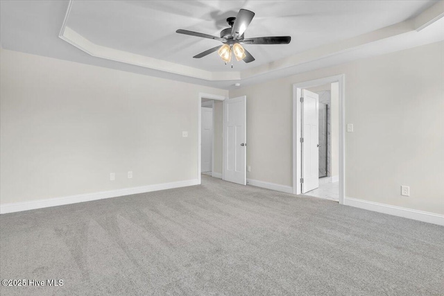 empty room featuring light colored carpet, ceiling fan, baseboards, and a raised ceiling