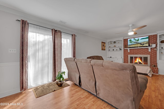 living room featuring ceiling fan, built in features, light wood-type flooring, and a brick fireplace