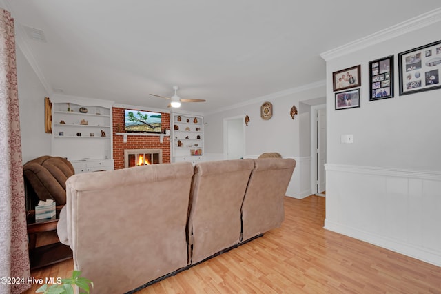 living room with a brick fireplace, crown molding, built in features, and light hardwood / wood-style flooring