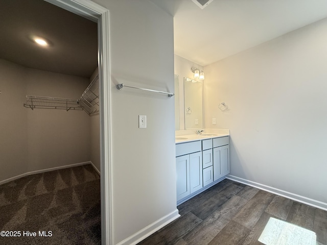 bathroom featuring a spacious closet, double vanity, wood finished floors, and baseboards