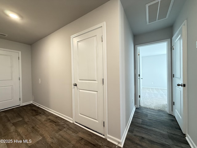 hallway featuring dark wood finished floors, visible vents, and baseboards