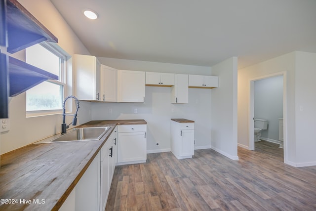 kitchen featuring butcher block countertops, white cabinets, sink, and light hardwood / wood-style flooring