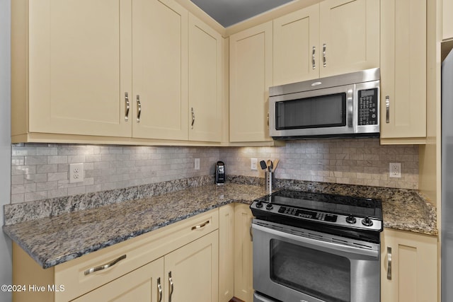 kitchen with tasteful backsplash, cream cabinets, dark stone counters, and stainless steel appliances