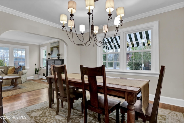 dining space featuring baseboards, arched walkways, wood finished floors, and crown molding